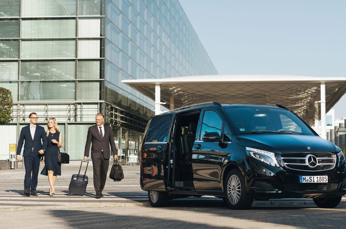 Chauffeur privé accueillant un passager avec pancarte nominative au terminal de l'aéroport CDG devant une Mercedes Classe S